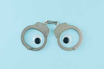 Handcuffs and eyes on isolated pastel blue background. The idea of fear of losing freedom. Minimal...