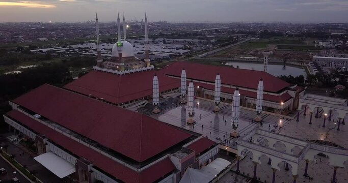 Moving drone shot of the great Mosque of Central Java (MAJT) in suset time. Th sun is orange and the weather is cloudy. It have some pillars and some umbrela that is closed