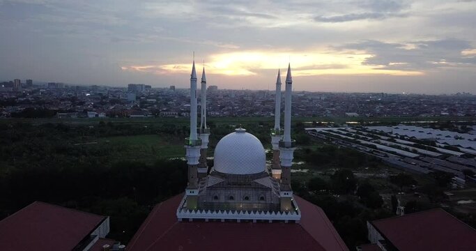 Reversing drone shot of the great Mosque of Central Java (MAJT) in suset time. Th sun is orange and the weather is cloudy. It have some pillars and some umbrela that is closed