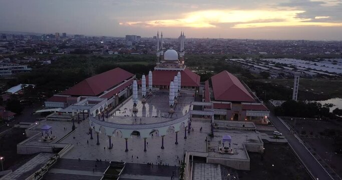 Orbit drone shot of the great Mosque of Central Java (MAJT) in suset time. Th sun is orange and the weather is cloudy. It have some pillars and some umbrela that is closed