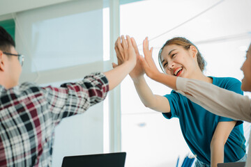 A group of creative young Asians in casual wear join hands to celebrate the success of their office project. Many men and women stood together at the beginning. teamwork concept of colleagues