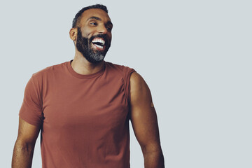 portrait mid adult bearded vaccinated man with plaster on arm laughing looking away at copy space...