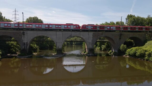 Red passenger train crossing a brick trestle in Germany on a sunny spring day. Static wide angle view