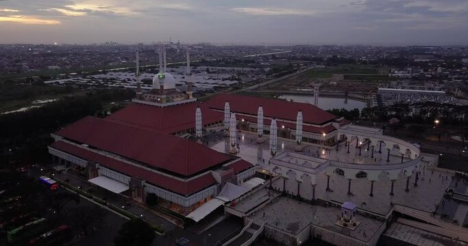 Reveal drone shot of the great Mosque of Central Java (MAJT) in suset time. Th sun is orange and the weather is cloudy. It have some pillars and some umbrela that is closed