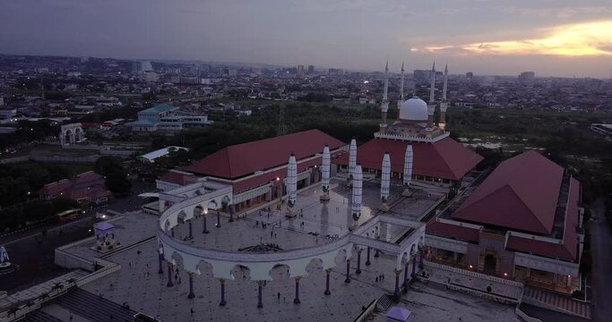 Sliding drone shot of the great Mosque of Central Java (MAJT) in suset time. Th sun is orange and the weather is cloudy. It have some pillars and some umbrela that is closed