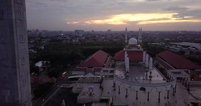 Rule of third composition drone shot of the great Mosque of Central Java (MAJT) in suset time. Th sun is orange and the weather is cloudy. It have some pillars and some umbrela that is closed