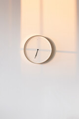 Still life, clock hanging on white wall, sunset rays falling