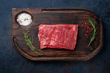 Raw flank steak on a wooden board with grilling seasonings