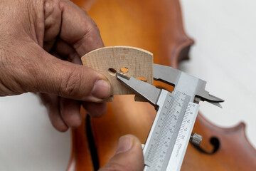Hands of an unrecognizable Latin American luthier taking precise measurements of a violin bridge...