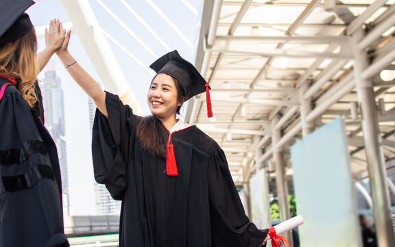 Two asian female students wearing uniform, cap and smiling with happiness, give high five or tag hands to celebrate after graduation. Education Concept.