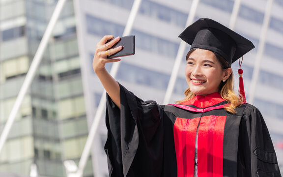 Young Asian female beautiful student graduated bachelor degree are taking selfie alone by using mobile phone while standing outdoor. Education and Technology Concept.
