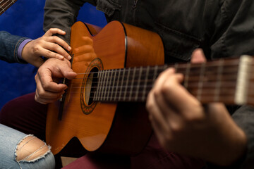 Fototapeta premium Unrecognizable Latin American teacher corrects right hand posture on guitar strings. Concept music lessons
