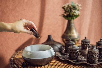Woman adding essential oil to aroma diffuser on table