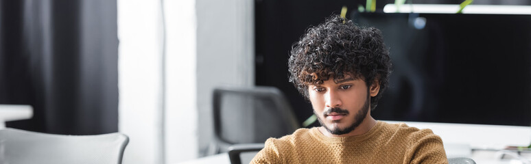 young and curly indian man working in advertising agency, banner.