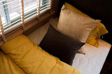 single bed mattress with yellow beige colour pillow arrange next to wooden shutter blind shade and...