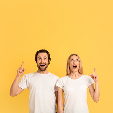 Cheerful shocked young caucasian man and woman in white t-shirts with open mouths show fingers up on empty space