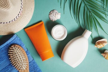 Summer travel beach essentials flat lay photography. Straw hat, towel, shampoo, sunscreen tube, wooden comb, palm leaves and seashells. Natural cosmetic products for hair and skin care