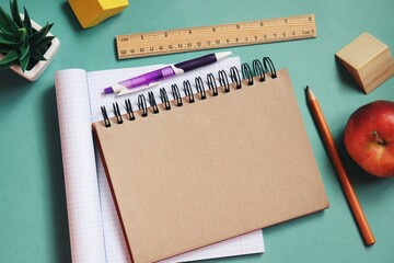 Back to school concept flat lay composition photography. Paper notebook, purple pen, pencil, wooden ruler and red apple on a green table. Mockup, free space for text