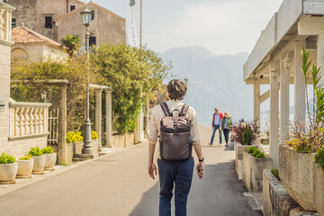Fototapeta na wymiar Man tourist enjoying Colorful street in Old town of Perast on a sunny day, Montenegro. Travel to Montenegro concept. Scenic panorama view of the historic town of Perast at famous Bay of Kotor on a
