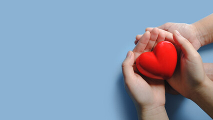 Adult and child hands holding red heart on blue background, Family hands holding heart, Health insurance, Organ donation, World heart day, Mental health day, Volunteer charity
