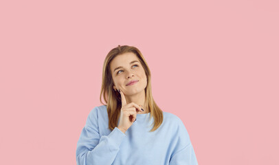 Portrait of smiling young thoughtful woman who has cool idea or came up with something interesting. Cheerful woman with finger on her cheek slyly looks away on pastel light pink background. Banner.
