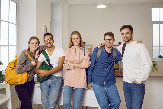 International education. Group portrait of happy and positive multiracial university friends posing in classroom. Five smart international students in casual clothes smile together and look at camera.