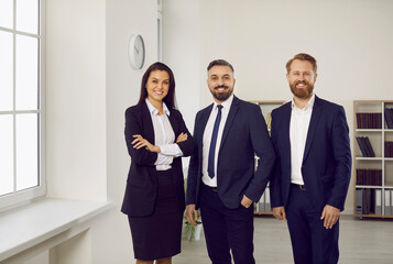 Portrait of professional and successful team of business or lawyers posing together in modern office. Two men and one woman dressed in stylish business attire are smiling while looking at camera.