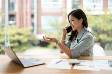 Corporate Communication. Asian Businesswoman Talking On Mobile Phone Working On Laptop In Modern Office.