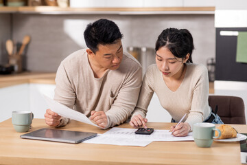 Asian couple counting monthly expenses, kitchen interior