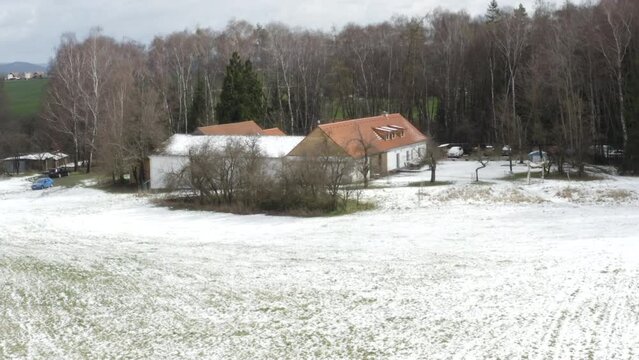 Farmhouse with snowy fields and leafless trees in winter countryside.