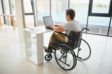 Middle age woman using laptop sitting on wheelchair at home