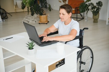 Positive elderly woman in wheelchair working on laptop, IT freelancer, online