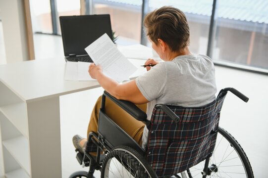 Positive elderly woman in wheelchair working on laptop, IT freelancer, online