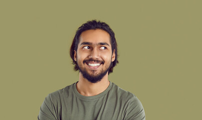 Man feels uncomfortable and looks to side. Head shot bearded mustached South Asian guy experiencing awkward moment. Funny guy likes something, admires someone, casts secret glance sideways and smiles