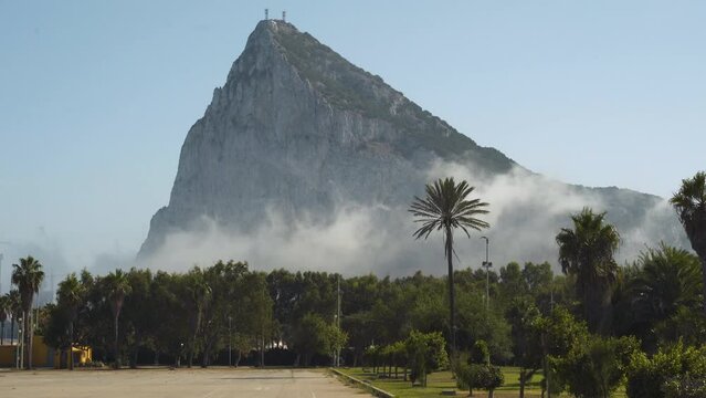 Rock of Gibraltar mountain above palm trees and thick smoke clouds.