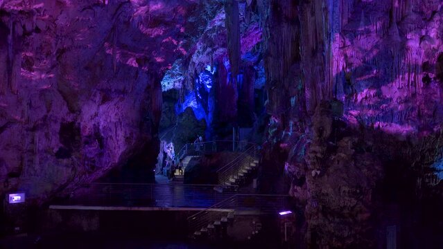 Tourists entering chamber of St. Michael's cave lit by purple light.