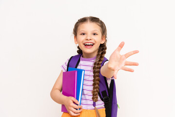 A little girl with a backpack and books pulls her hand forward on a white isolated background. The child invites you to the courses.