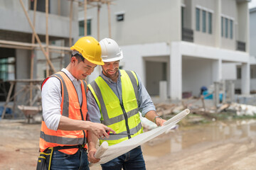 Asian male civil engineer and caucasian male architect wears safety vest with helmet discuss and...