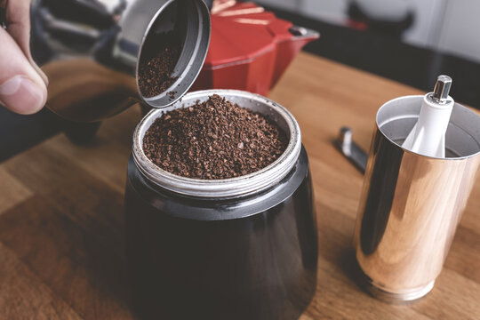 A man is grinding coffee beans in a manual coffee grinder for an Italian coffee pot