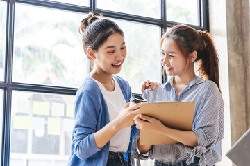 Two Asian business managers standing at spacious open plan office and sharing ideas concerning start-up project.
