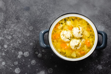Chicken meatball soup in pot on dark background. Top view, copy space, flat lay.