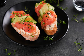Sandwiches. Salmon toast with cream cheese, cucumber, black sesame and microgreens on black background. Seafood. Healthy food. Photography in low key. Top view.