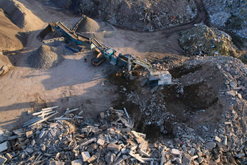 Excavator at landfill the load concrete waste in a mobile jaw crusher machine. Disposal of construction waste. Recycling concrete and asphalt from demolition. Re-use concrete after demolition.