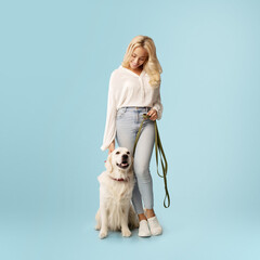 Friendship concept. Happy woman posing with her happy labrador dog on a leash, standing on blue...