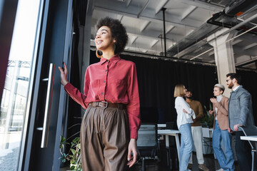 low angle view of positive african american advertising agent looking away near interracial colleagues in office.