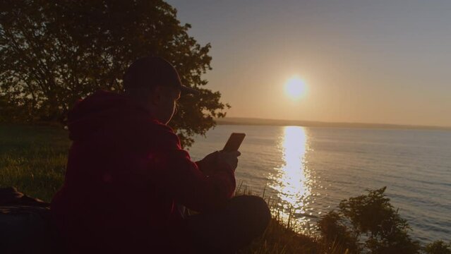 Man uses a smartphone while sitting on the seashore while traveling.