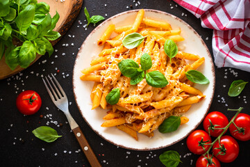 Italian pasta with tomato sauce, basil and parmesan cheese on dark table.