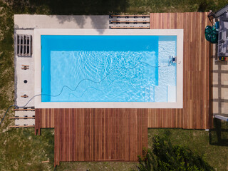 aerial drone flight over beautiful green garden with pool and the wooden deck of the pool is in progress and pool robot is working right now in the water