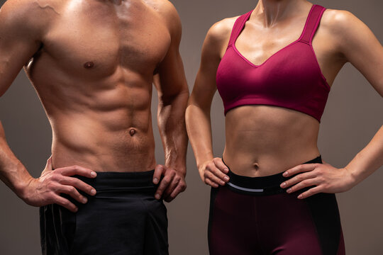 Cropped view of the athletic man and woman posing to the camera before fitness exercise at the studio with brown wall