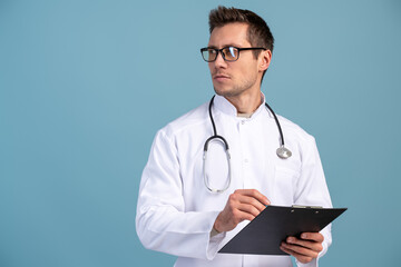 Fototapeta premium Waist up portrait view of the confident doctor in a uniform and in glasses holding folder and looking away with serious face. Stock photo